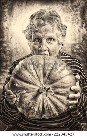 Halloween theme. Portrait of an old woman eating a big ripe pumpkin freshly harvest in autumn. Studio shoot and sepia toned image.