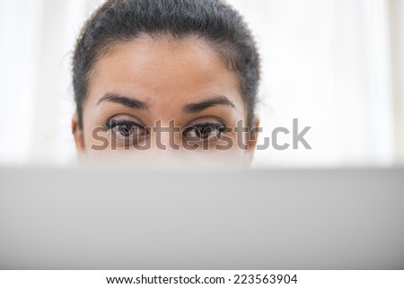Facial expression of concentration. Brown woman\'s eyes working behind her display computer. Sparse and copy space