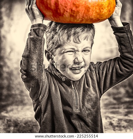 Closeup of little boy making a face with heavy orange pumpkin hat. Halloween theme. Studio shoot after freshly harvest in autumn. Mixed sepia and color image