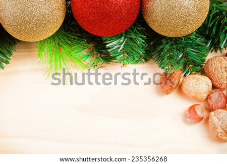 Christmas balls with green fir-tree branches and nuts on wooden background. Space for text