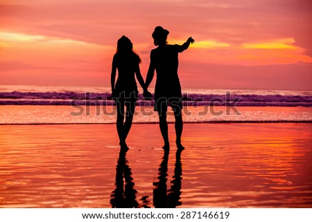 Silhouettes of young couple in love having a great time on the honeymoon staying on the beach with beautiful red sunset on background