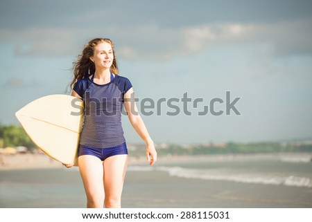 Beautiful sexy surfer girl on the beach at sunsetwalks along ocean shore with yellow surfboard in her hands in sunset light. Healthy life, sport  concept with copyspace