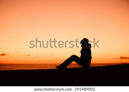 Silhouette of a woman in coat sitting on the edge with beautiful red sunset on background. Peace, cerenty, lifestyle concept