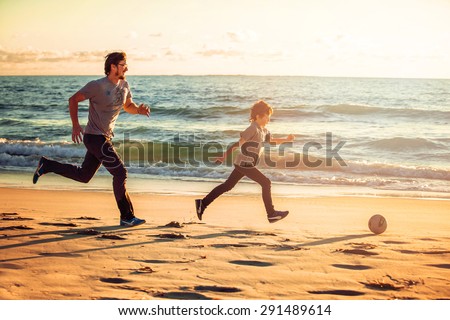 Happy father and son play soccer or football on the beach on sunset having great family time on summer holidays. Lifestyle, vacation, happiness, joy concept