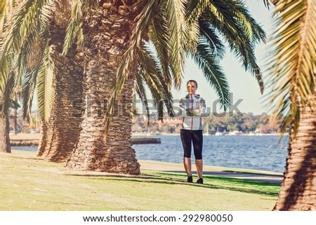 Healthy lifestyle young sporty woman having break between palm trees after jogging at tropical park on sunny summer day