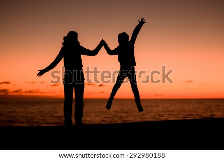 Silhouette of a young mother and her jumping son in front of a red sunset in the sky on a summer day on holidays