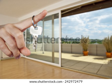Apartment key on the finger of a hand in the interior of an empty apartment.