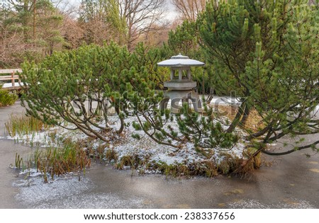 Decorative island with a Japanese stone lantern in the pond in the Japanese garden at the beginning of winter and the first snow