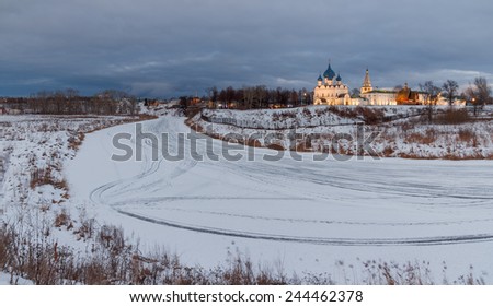Winter landscape in overcast evening in the old Russian town Suzdal through the river Kamenka with temples and buildings of the Kremlin