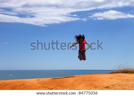 young woman jumps with arms wide open at the coast