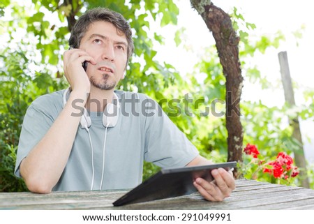 young man at the phone and tablet pc with headphones, outdoor
