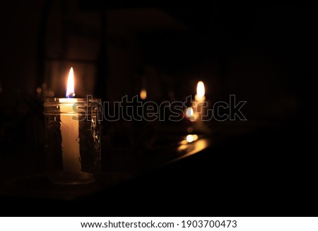 Candles on kitchen counter during power outage. 2 candles are inside a mason jar. Pitch black room except the candle lights. Selective focus on first candle with bokeh lights in the back.  商業照片 © 