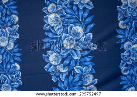 Vintage Polynesian/Hawaiian cloth fragment with faded blue and white flowers on a black background.
