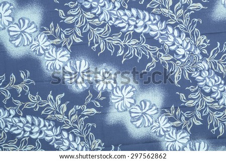 Vintage Hawaiian cloth fragment with white plumeria flowers and blue green leaves on a faded blue background.