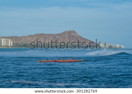 Honolulu, Hawaii, USA, July 30, 2015:  Outrigger canoe and team surf a late evening wave into the Ala Wai Channel with Diamond Head in the background.  Outrigger canoes are increasingly popular.