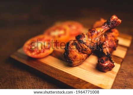 Close up of roasted chicken drumsticks decorated on wooden plate along with fresh, juicy tomatoes. Dramatic image of non vegetarian food with copy space for text. Stock fotó © 