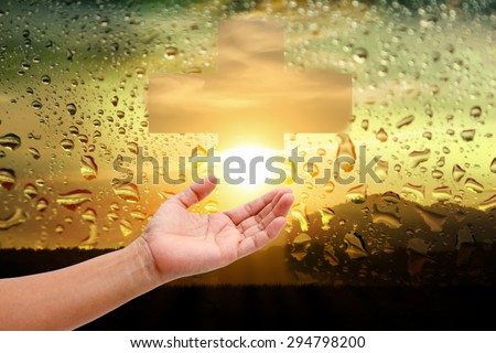 women hand touch the cross and pray at  water drops on sunset mirror background.