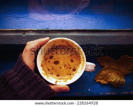Hand in winter sweater holding a cup of coffee near the window. Hot coffee for cold weather