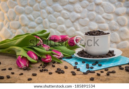 Coffee beans in a cup with pink tulips on wooden table