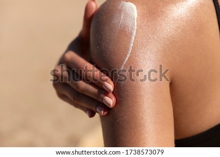 Young woman applying sun cream or sunscreen on her tanned shoulder to protect her skin from the sun. Shot on a sunny day with blurry sand in the background Stok fotoğraf © 