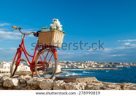 Old red bicycle set in a wall along the seafront of Syracuse, Sicily, and the town in the distance