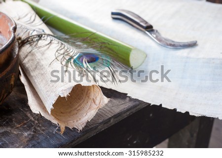 Rolled up papyrus paper leaf, a cut section of the plant, a colored quill pen and the typical working knife laid on a papyrus layer