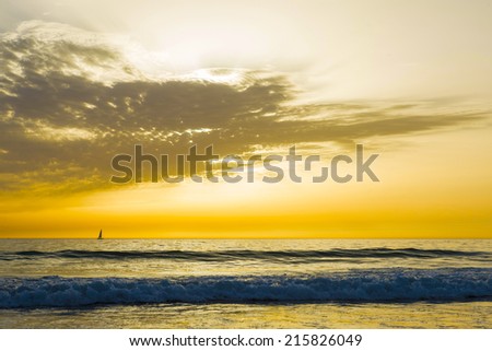 sunset on a beach in Andalusia, Spain, with a sailboat on the horizon