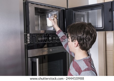 Young boy warming a glass of milk in the microwave