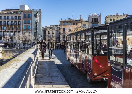 Girona, Spain - December 28, 2014: People walking and a tourist tram on an old stone bridge over the Onyar river