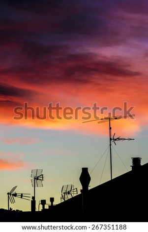 Silhouettes of antennas and chimneys backlit at sunset with colorful sky clouds