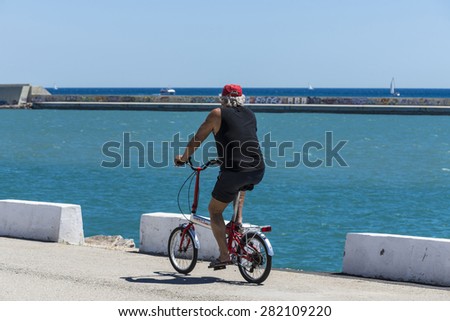 Barcelona, Spain - May 23, 2014: Pensioner riding a bicycle on a breakwater of the port of Barcelona