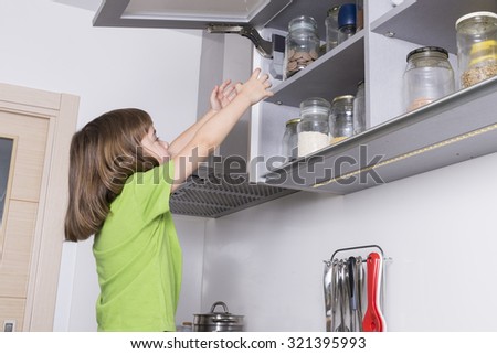 Little girl on a chair to reach higher to get chocolate in the kitchen