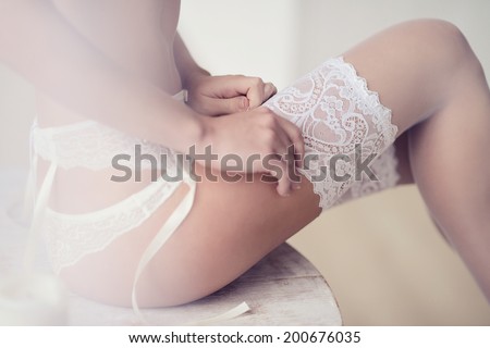 Beautiful model in white lace lingerie. Close-up of a female buttocks on the table. Girl in panties, belt, and stockings. Hosiery underwear. Portrait of sexy fashion woman with attractive ass