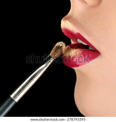 Golden lips. Fashion model girl with perfect bright color makeup. Beautiful woman with red glossy lips. Close-up of burgundy lips. Isolated on black background. Open sexy mouth. Brush of makeup artist