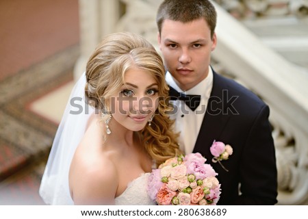 Beautiful sexy model girl in white dress. Wedding couple. Man in suit. Beauty blonde bride with brunette groom. Female and male portrait with bouquet. Woman with lace veil. Cute lady and guy indoors