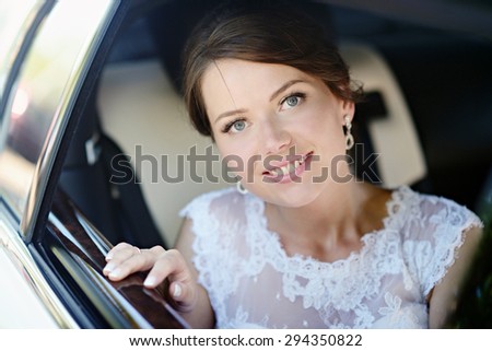 Beauty bride in bridal gown with lace veil in the car. Beautiful model girl in a white wedding dress. Female portrait in the auto. Woman with hairstyle. Cute lady outdoors