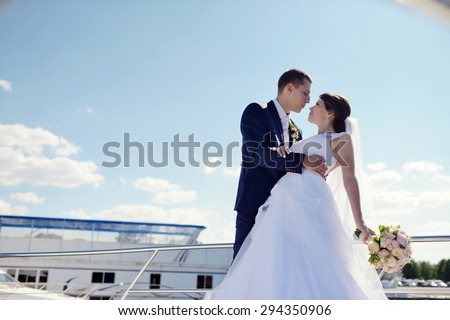 Wedding couple is hugging on a yacht. Beauty bride with groom. Beautiful model girl in white dress. Man in suit. Female and male portrait. Woman with lace veil. Cute lady and guy outdoors