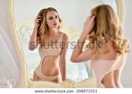 Beautiful sexy lady in elegant white bodysuit. Portrait of fashion model girl indoors. Beauty blonde woman with attractive buttocks in lace lingerie. Female ass in underwear. Naked body