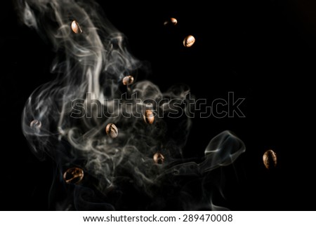 Coffee beans falling down trough smoke over black background - isolated