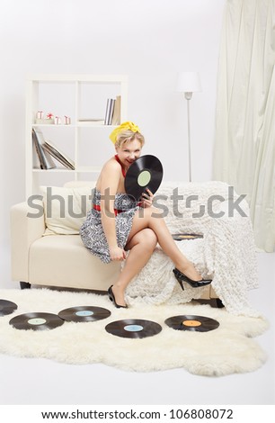 indoor portrait of beautiful young blonde size plus woman model sitting on sofa with vinyl records in interior