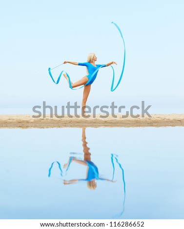 outdoor portrait of young beautiful blonde woman gymnast training with ribbon on the beach