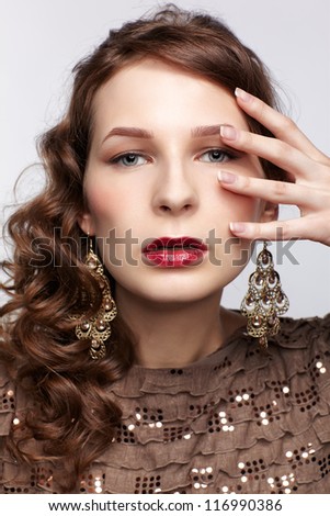 portrait of beautiful young brunette woman in ear-rings touching her face with manicured fingers