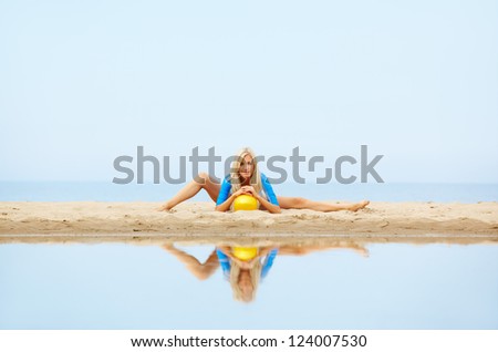 outdoor portrait of young beautiful blonde woman gymnast working out with ball on the beach