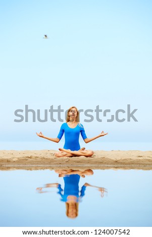 outdoor portrait of young beautiful blonde woman gymnast meditating in yoga lotus pose on the beach