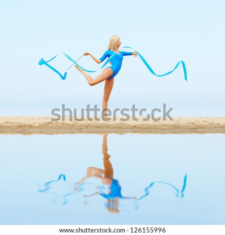 outdoor portrait of young beautiful blonde woman gymnast working out with ribbon on the beach