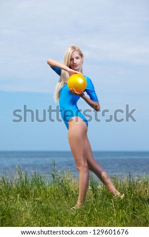outdoor portrait of young beautiful blonde woman gymnast working out with ball on grass