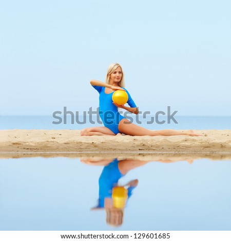outdoor portrait of young beautiful blonde woman gymnast training with ball on the beach