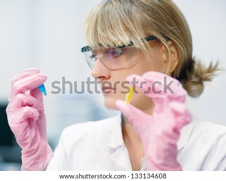 low focus portrait of young woman scientist in protective glasses and gloves comparing two test tubes