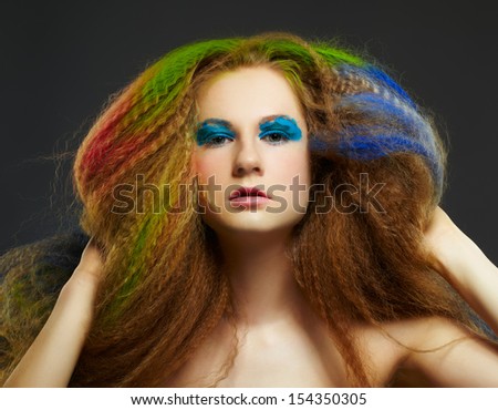 portrait of young beautiful redhead woman psoing on gray with long hair colored with blue green and red