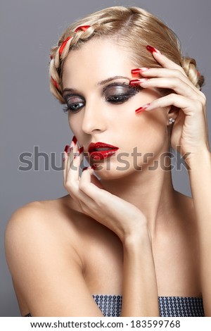 Young blonde woman with braid hairdo and red nails on gray background